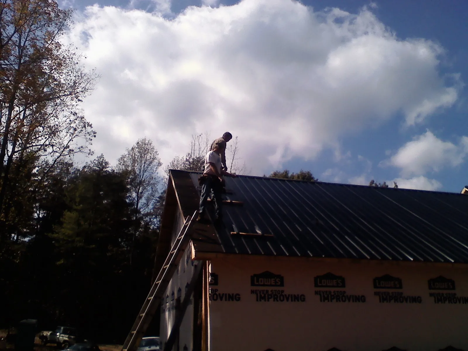 Roofer fastening dark metal panels high against a cloudy sky, from a Roof Inspection job in New Paris
